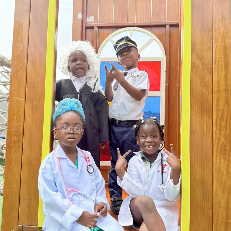 A young Elmwood International School student wearing a black chef's hat whisking ingredients in a large metal bowl with a smudge of flour on her forehead.